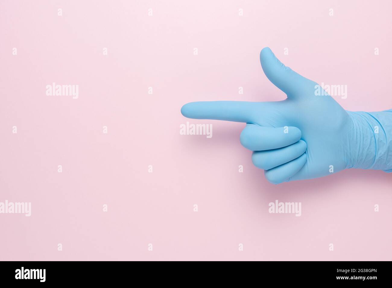 Hand in the blue glove depicts the gesture of a handgun on pink background. Minimal flat lay concept. Stock Photo
