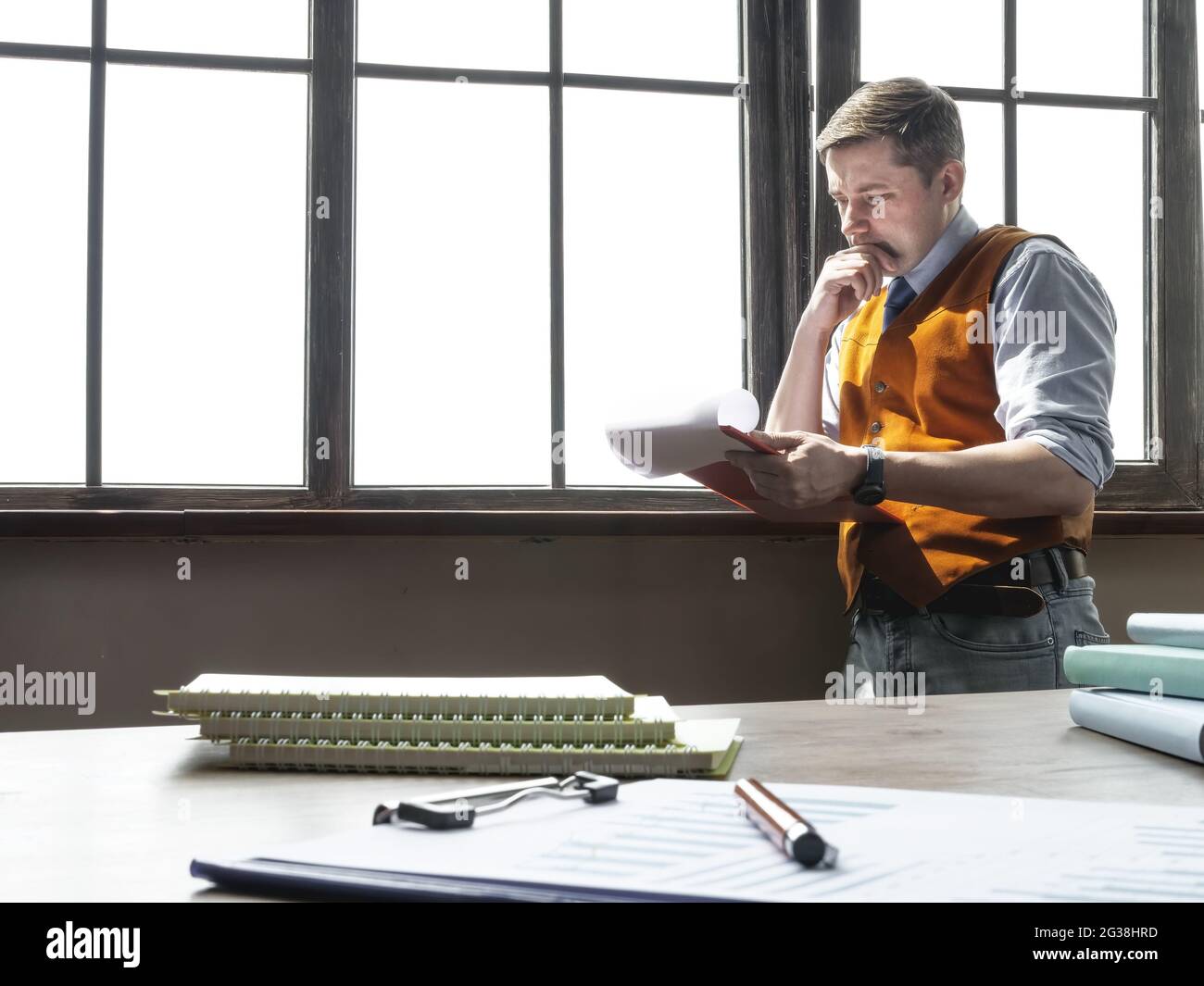 A businessman stands near the window and reads financial report. Stock Photo