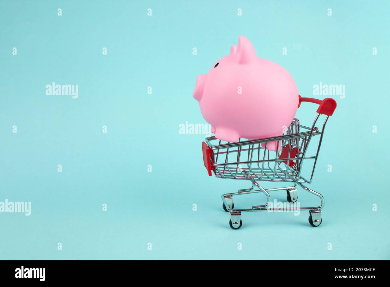 Pink piggy bank in mini shopping cart on blue background. Saving money for sales of the year, black friday concept Stock Photo