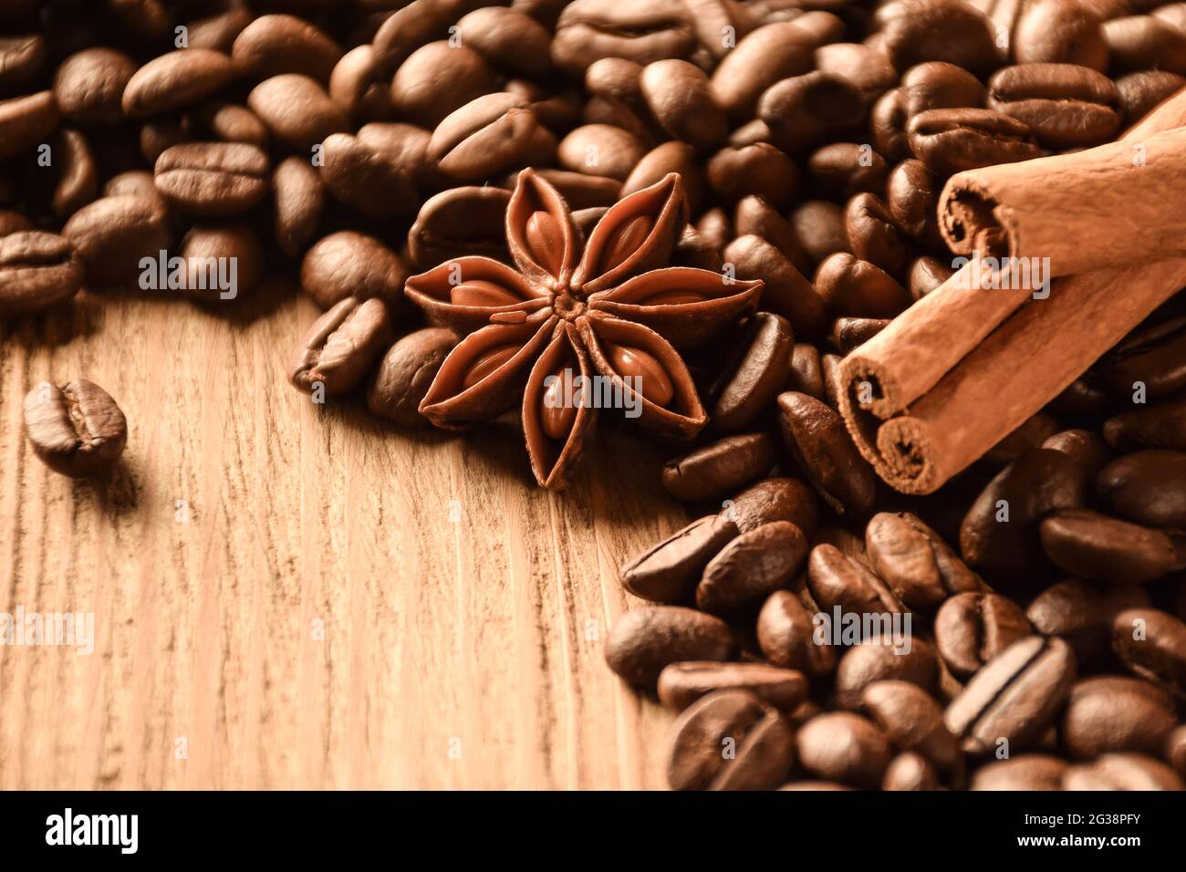 Anise, cinnamon and many coffee beans lie on a brown wooden table. There is an empty space at the bottom left. Stock Photo