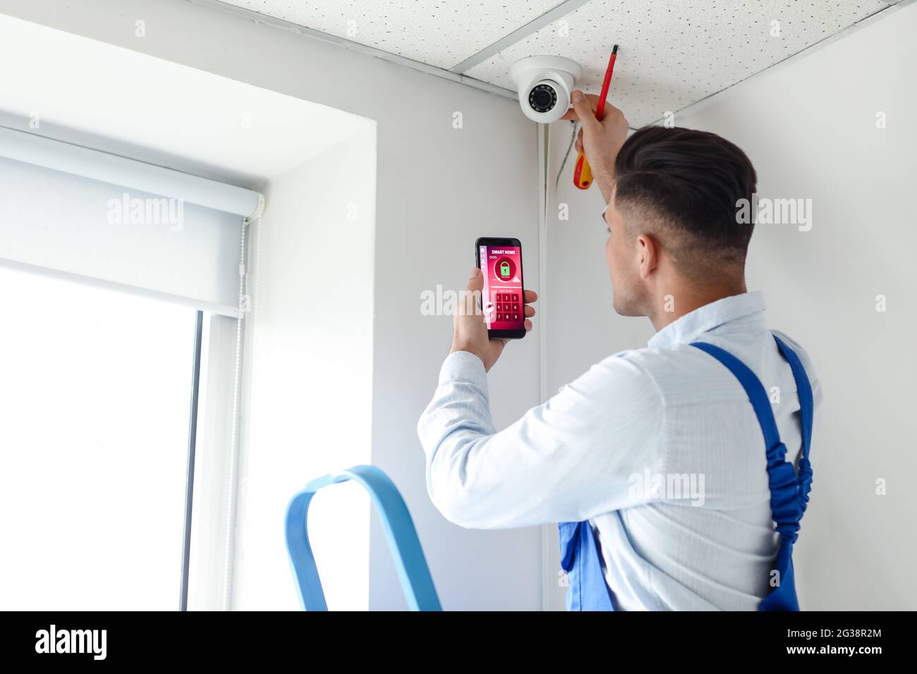 Worker with mobile phone checking alarm system indoors Stock Photo