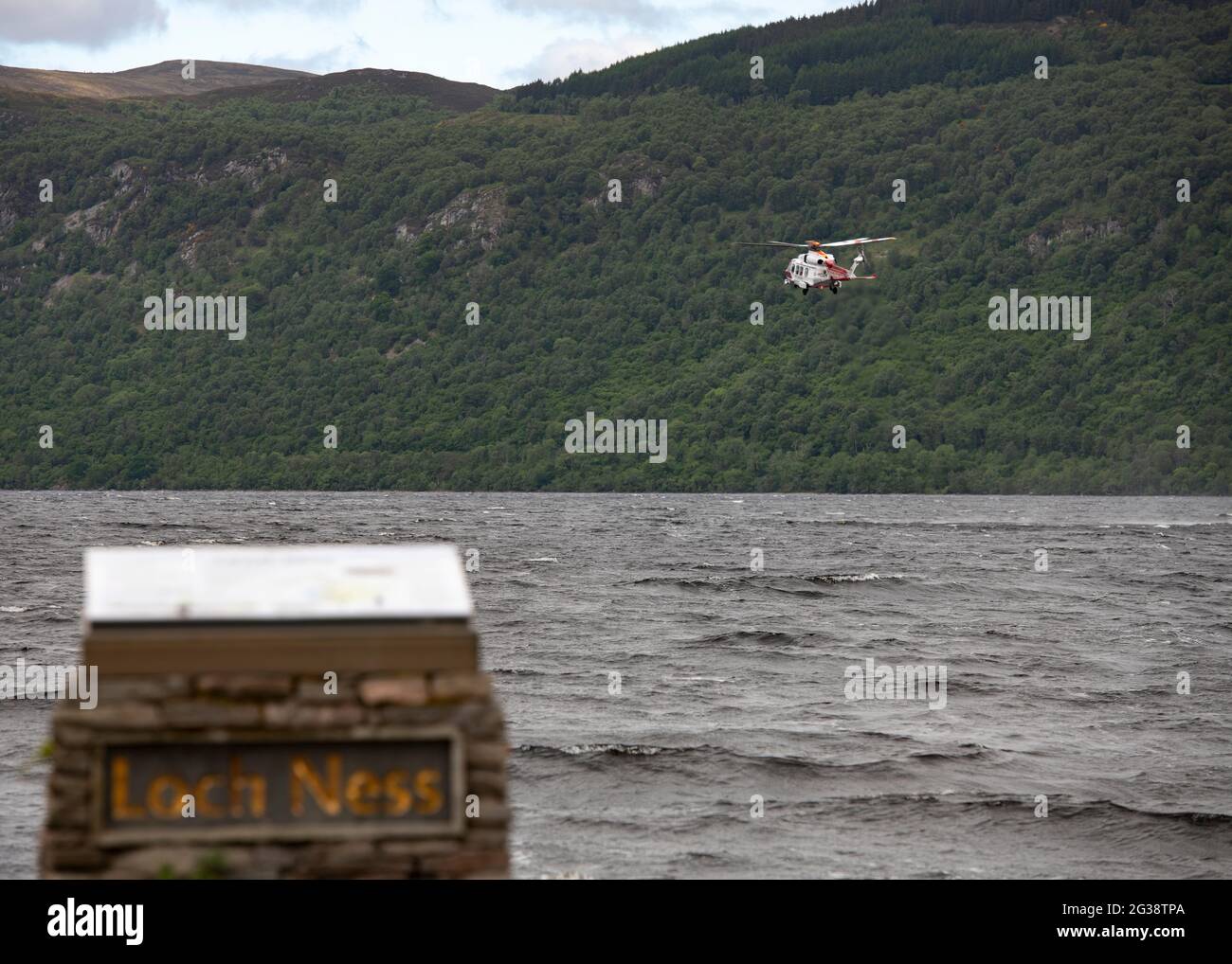Dores, Loch Ness, Scotland, UK. 14th June, 2021. Pictured: Coast Guard helicopter seen hovering above the deep and murky waters of Loch Ness where there have been many Loch Ness Monster sightings from Dores beach. The helicopter is seen lowering personnel into the loch to perform a water rescue from the airborne platform whilst hovering less than a hundred feet above the water surface. Credit: Colin Fisher/Alamy Live News Stock Photo