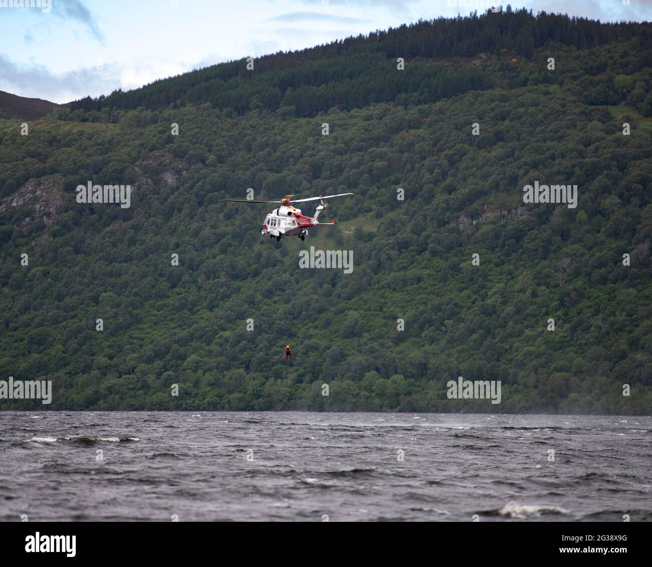 Dores, Loch Ness, Scotland, UK. 14th June, 2021. Pictured: Coast Guard helicopter seen hovering above the deep and murky waters of Loch Ness where there have been many Loch Ness Monster sightings from Dores beach. The helicopter is seen lowering personnel into the loch to perform a water rescue from the airborne platform whilst hovering less than a hundred feet above the water surface. Credit: Colin Fisher/Alamy Live News Stock Photo