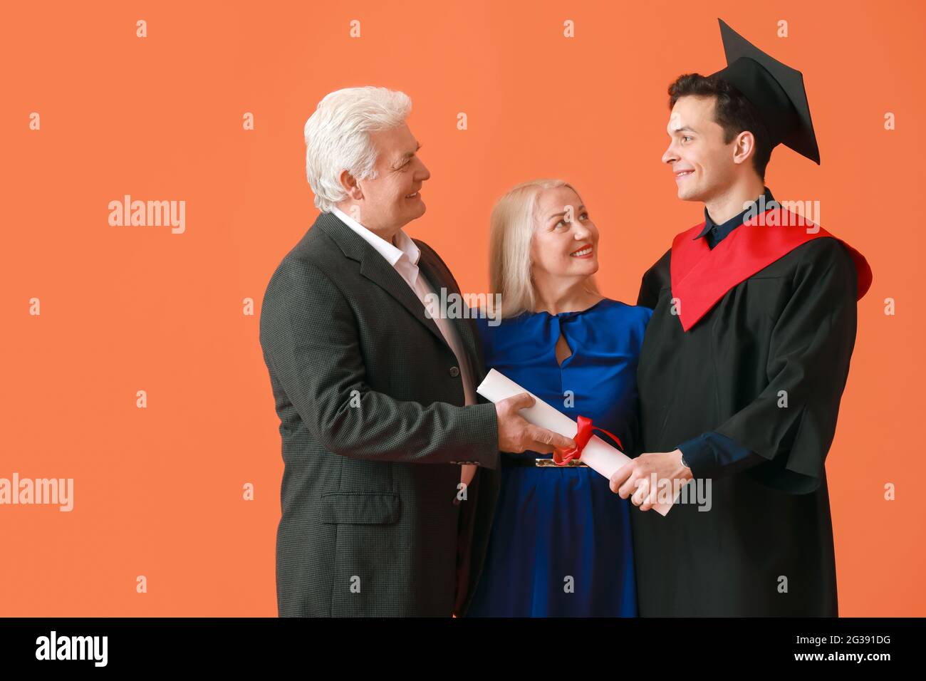 Happy male graduation student with his parents on color background ...