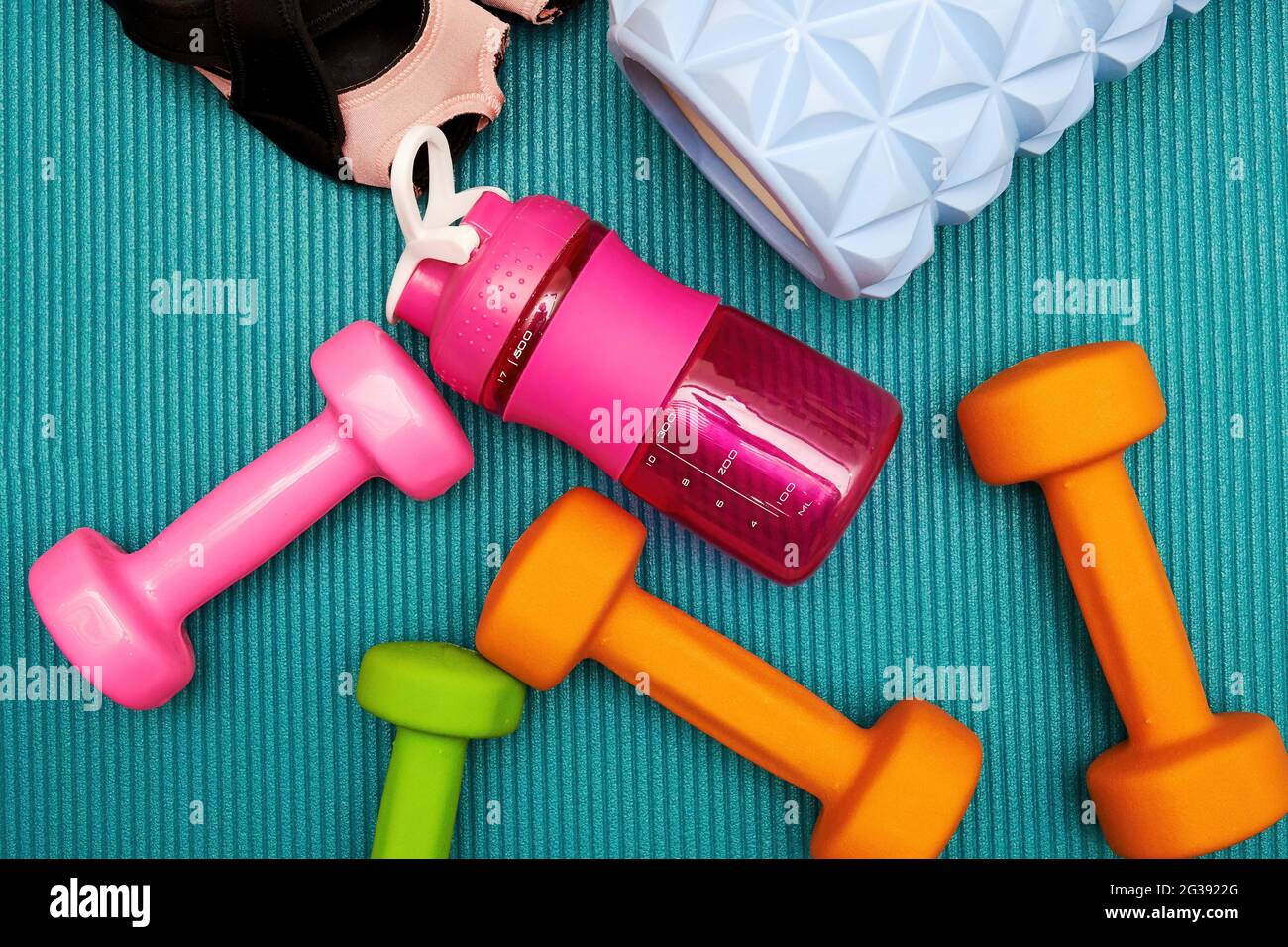 Women's fitness sneakers, dumbbell, roller, bottle, bricks scattered on the mat. Sports equipments and workout backgrounds Stock Photo