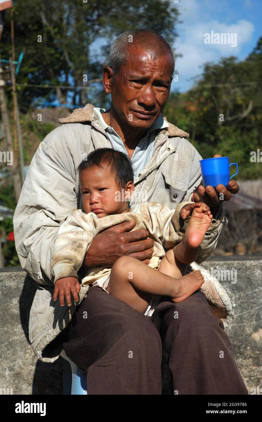 Yang Yiwang, in his old-age, cares for his grandchildren while his son, like many others who have acquired Thai citizenship, works in the city and sends money back to support the family. This is a new social value that is becoming the trend in Baan Tam-Ngob. Chiangmai, Thailand. December 10, 2007.. Stock Photo
