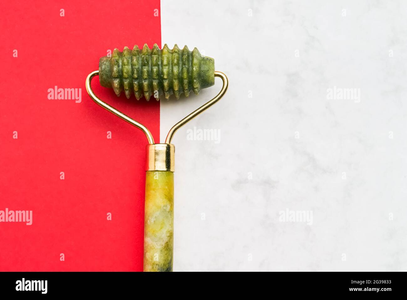 Green jade face roller on a red-white background. SPA concept. Top view, copy space for text Stock Photo