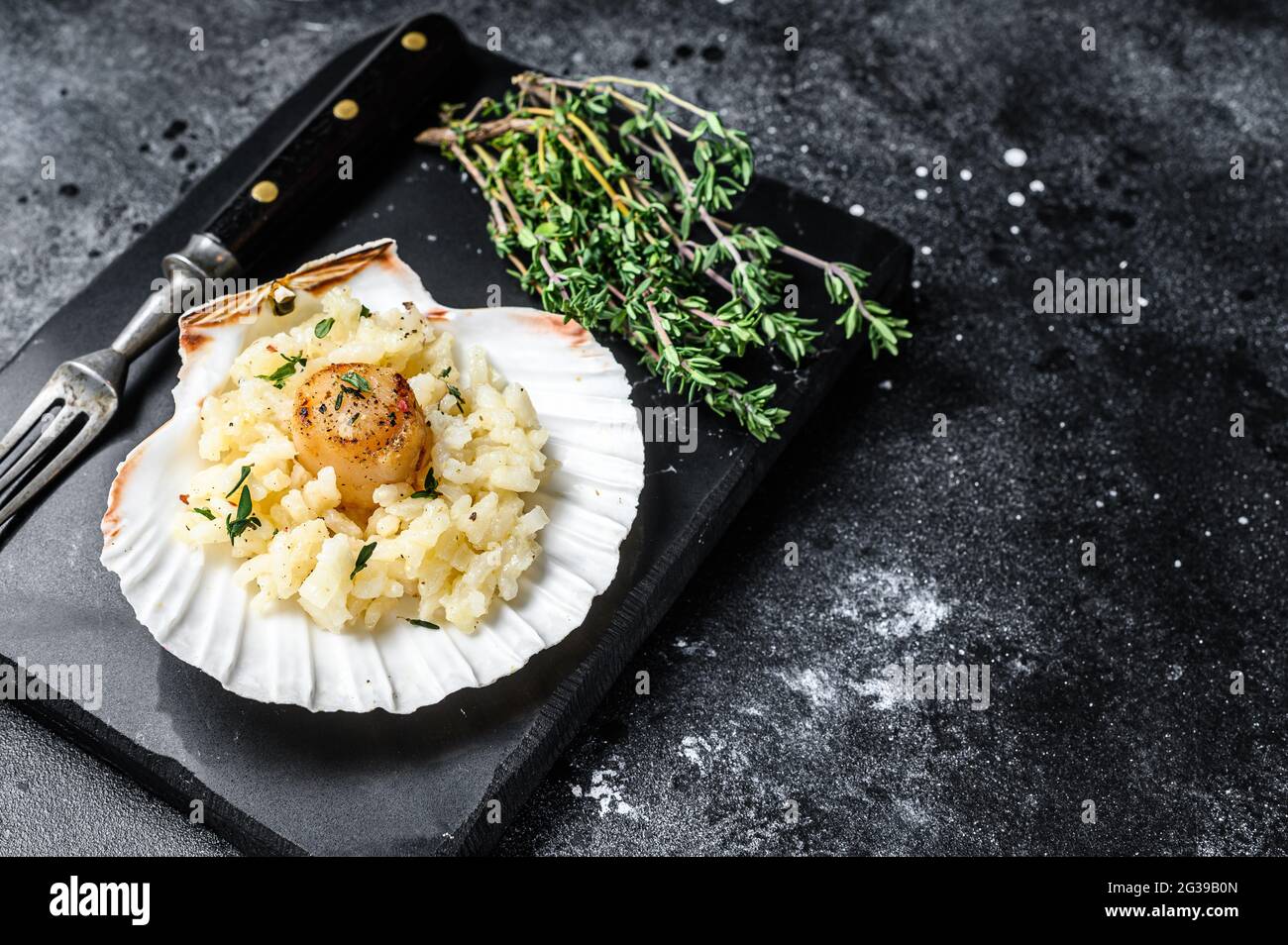 Risotto with pan seared sea scallops in a shell. Black background. Top ...