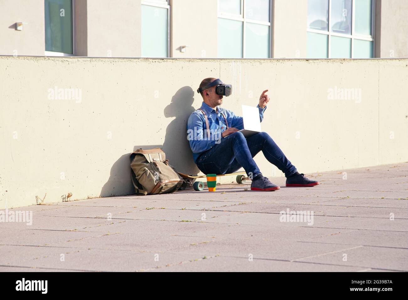 Businessman examining virtual reality simulator while using laptop in park Stock Photo
