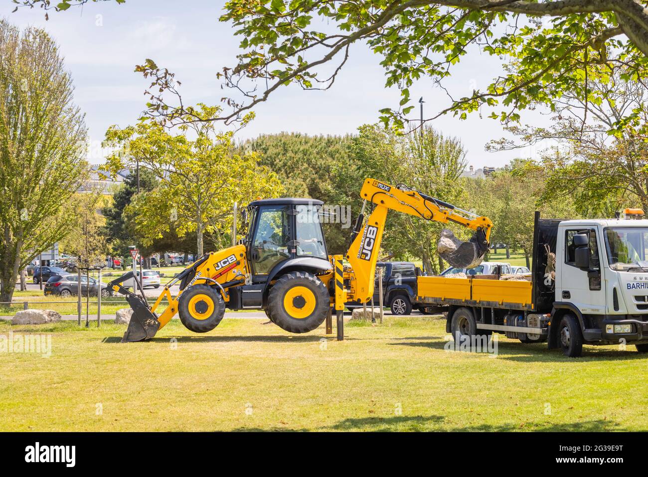 A yellow JCB 3CX Eco backhoe loader working in a park in Southsea, Portsmouth, Hampshire, south coast England raised on its supporting legs Stock Photo