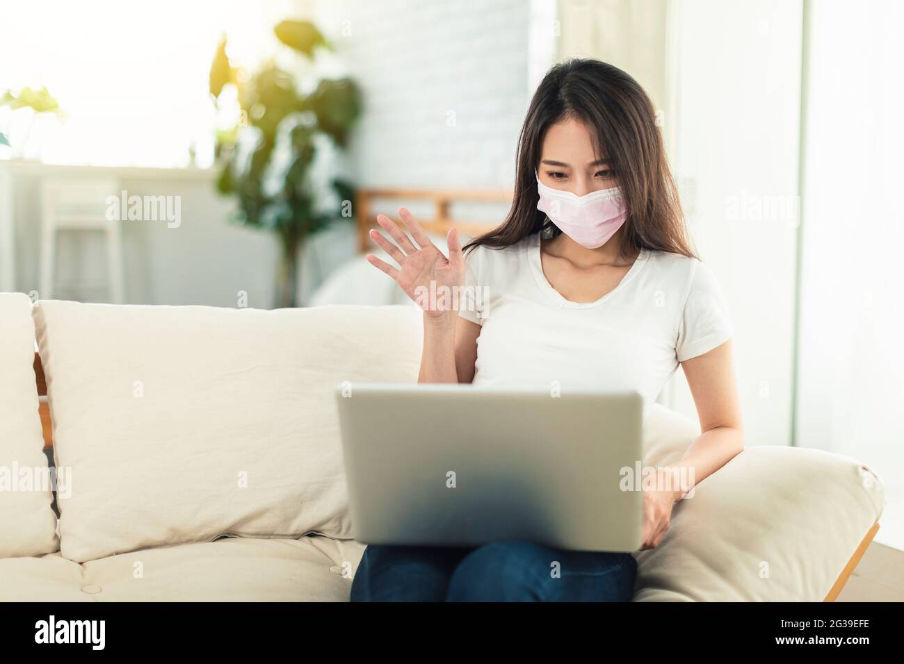 Young women working at home, wearing masks to protect themselves, sitting on the sofa using laptops for telecommuting, and video chatting with colleag Stock Photo