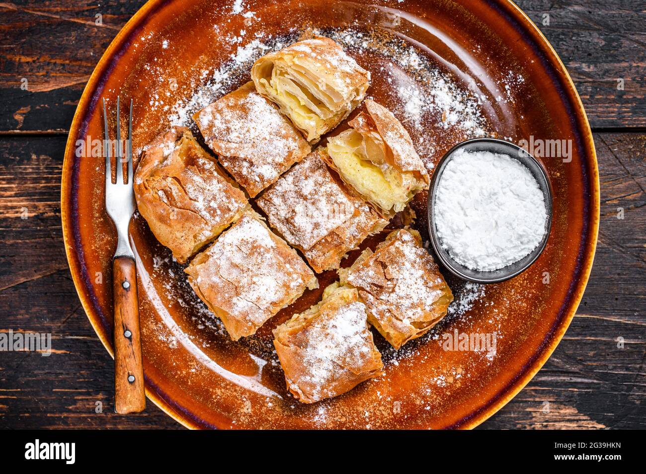 Sliced Greek Bougatsa pie with phyllo dough and semolina custard cream. Dark Wooden background. Top view Stock Photo