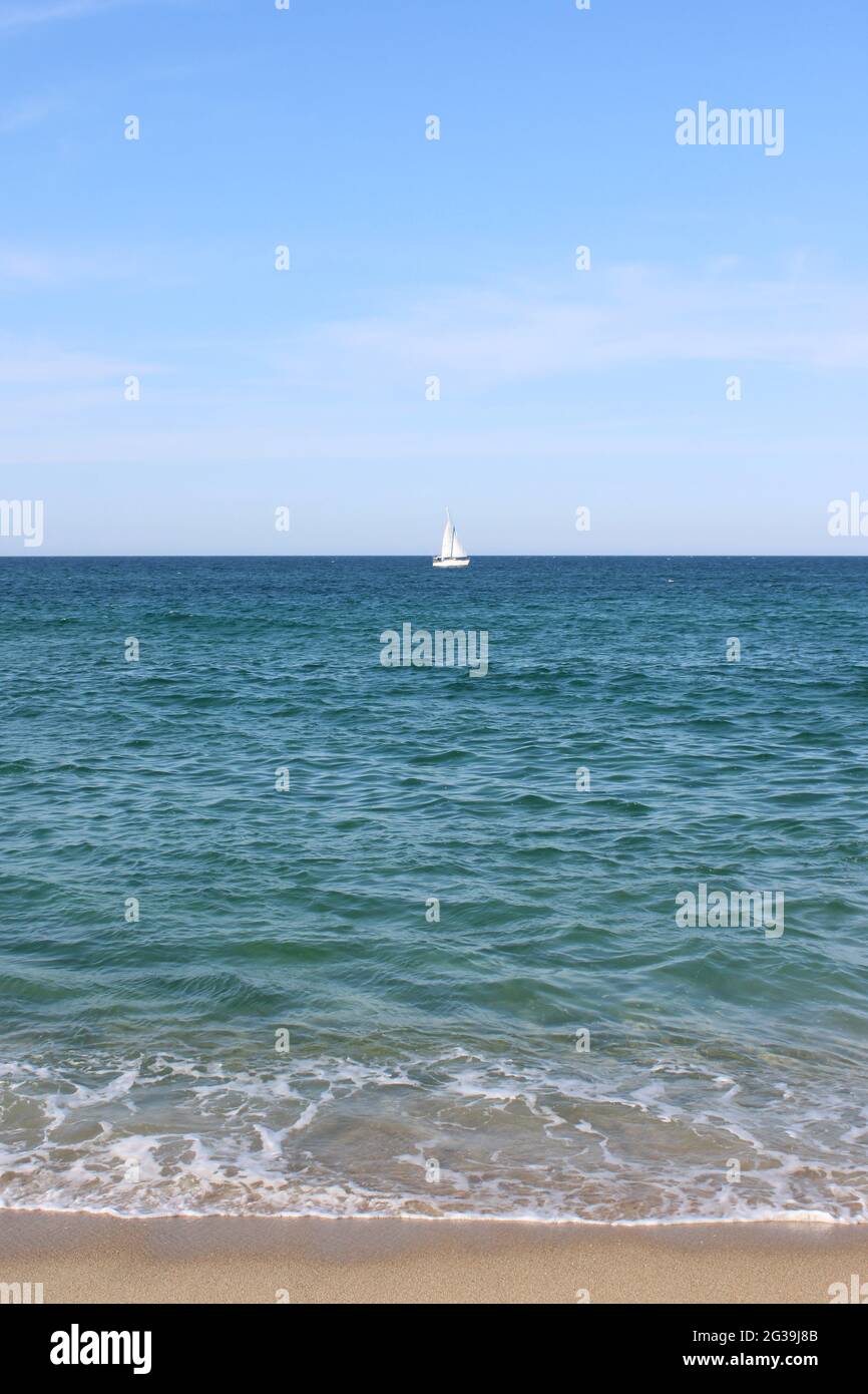 Seaside view of lone white sailboat on open water Stock Photo