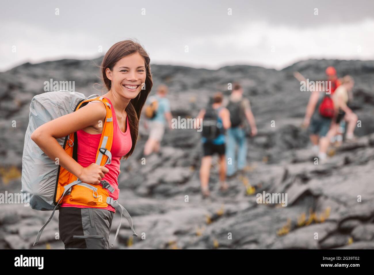 Hawaii volcano hike adventure happy Asian woman with backpack in Big Island, Hawaii. Hiking group of tourists walking on black lava field trail Stock Photo