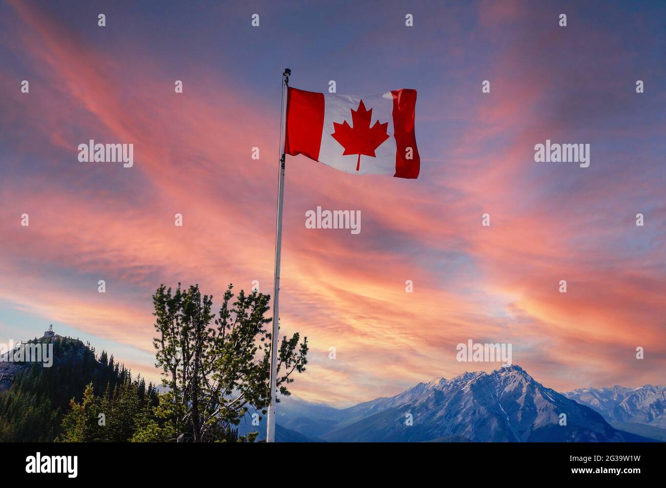 Canada flag flying atop Sulphur Mountain with sunset view of Banff National Park with Canadian Rockies in the background. Stock Photo