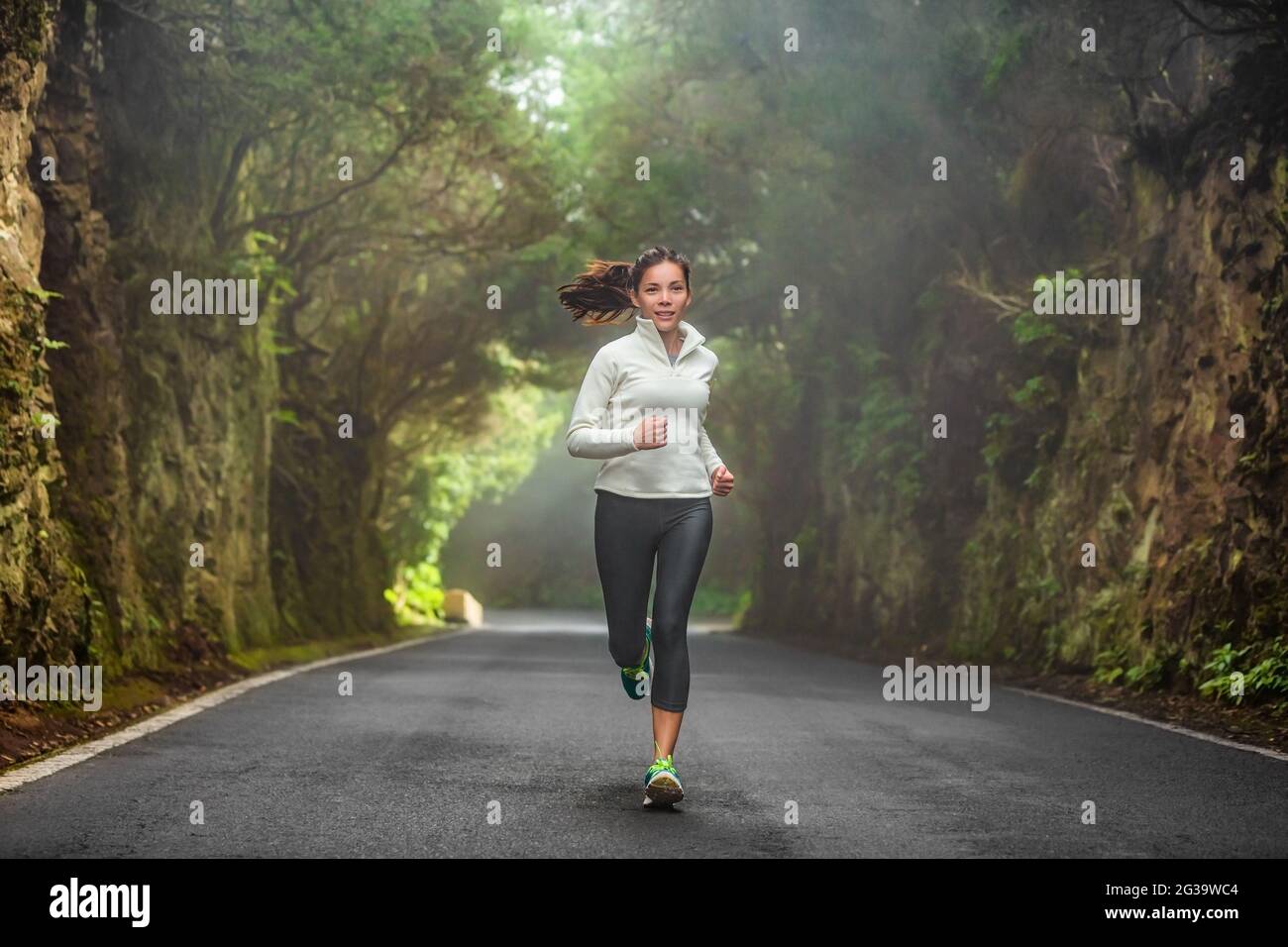 Running woman in autumn forest training on cold morning. Outdoor sport Asian girl athlete runner jogging outside fitness winter motivation Stock Photo