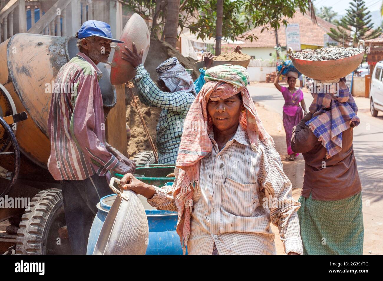 Female Indian manual labour workers carrying heavy loads on their heads at construction site, Agonda, Goa, India Stock Photo