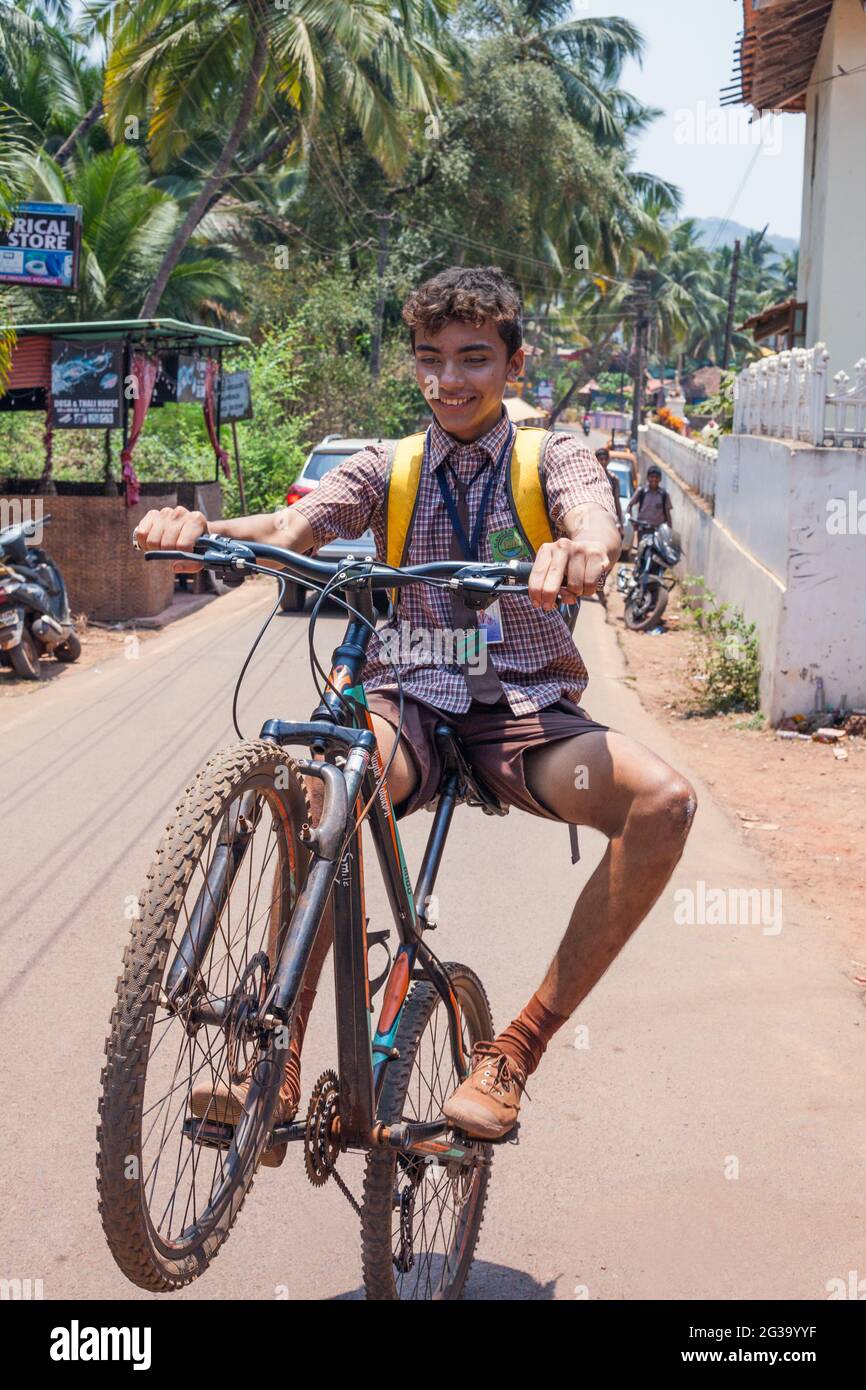 Young Indian schoolboy in uniform with curly hair performs wheelie on ...