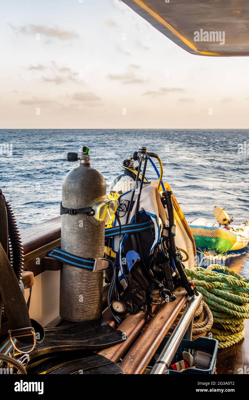 Diving gear with tanks, BCDs,  regulators, weight belts assembled, on a diving boat with sea view in the background, Red Sea, Sudan, portrait view. Stock Photo