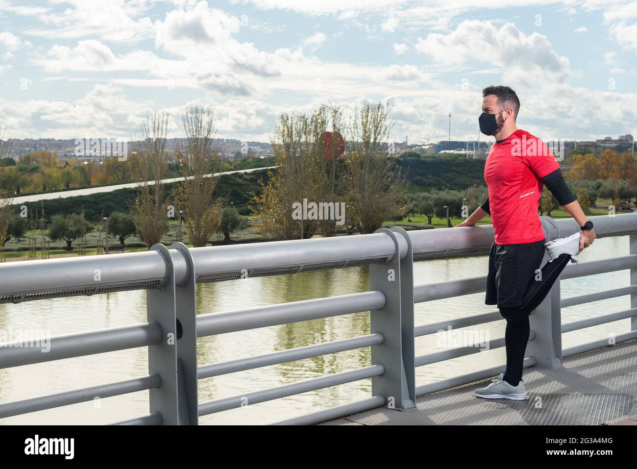 Young runner man with mask stretching in a park Stock Photo
