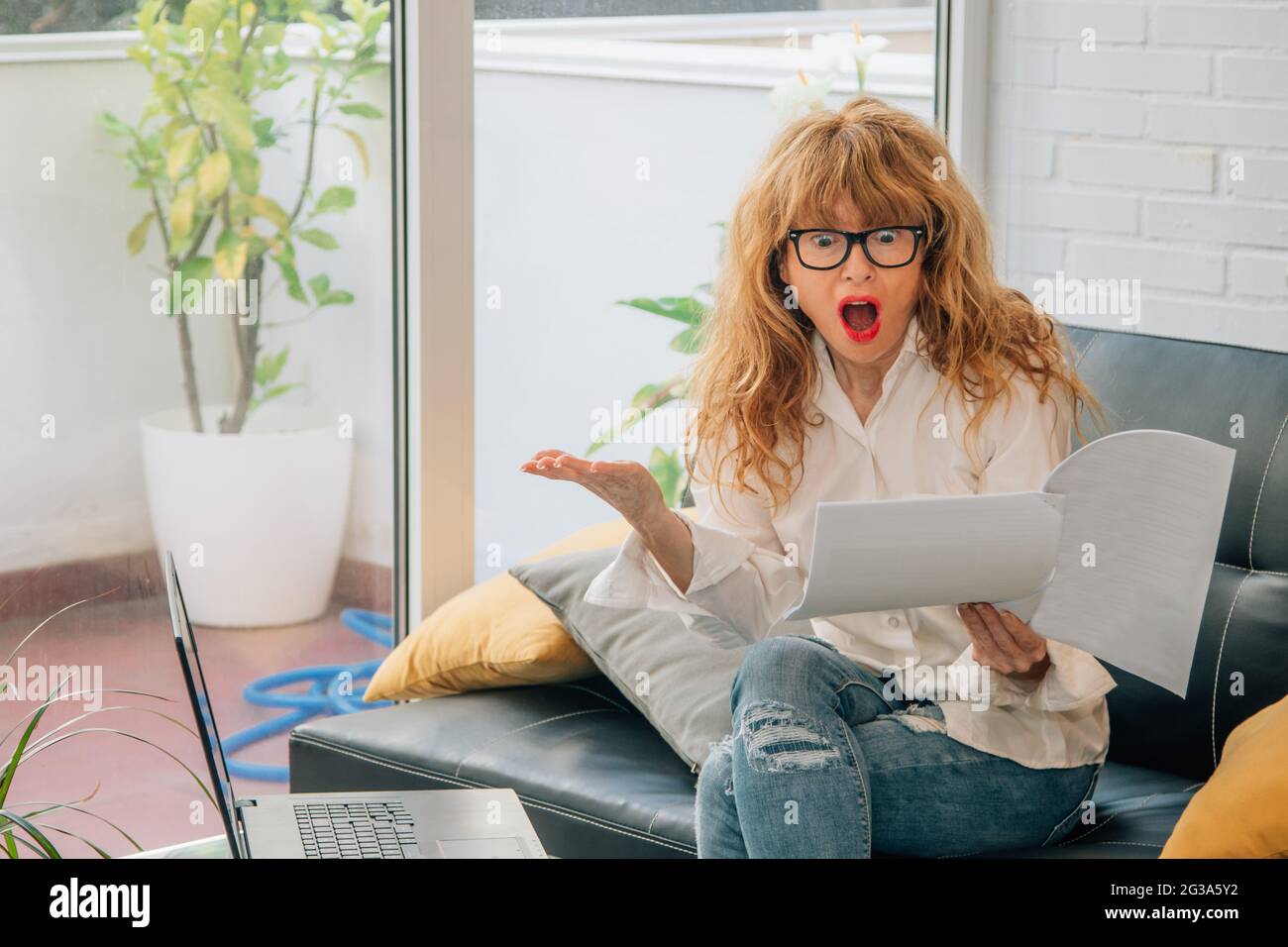 woman at home with computer surprised looking at papers Stock Photo