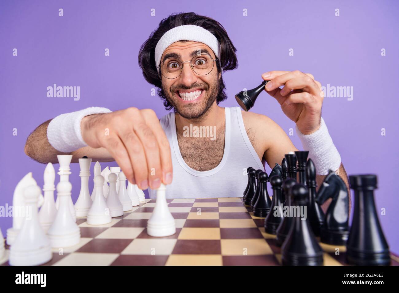 Photo of young happy cheerful smiling funky geek nerd man in glasses playing chess isolated on violet color background Stock Photo