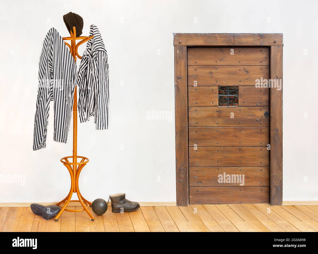 The striped prisoners costume hangs on the coat hook in an cell with door with a small window. Stock Photo