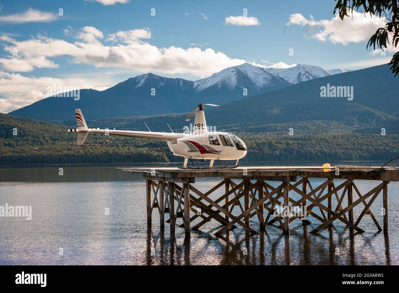 Tranquil scene, helicopter on a landing platform over a clear, calm lake with beautiful snow capped mountain background Stock Photo