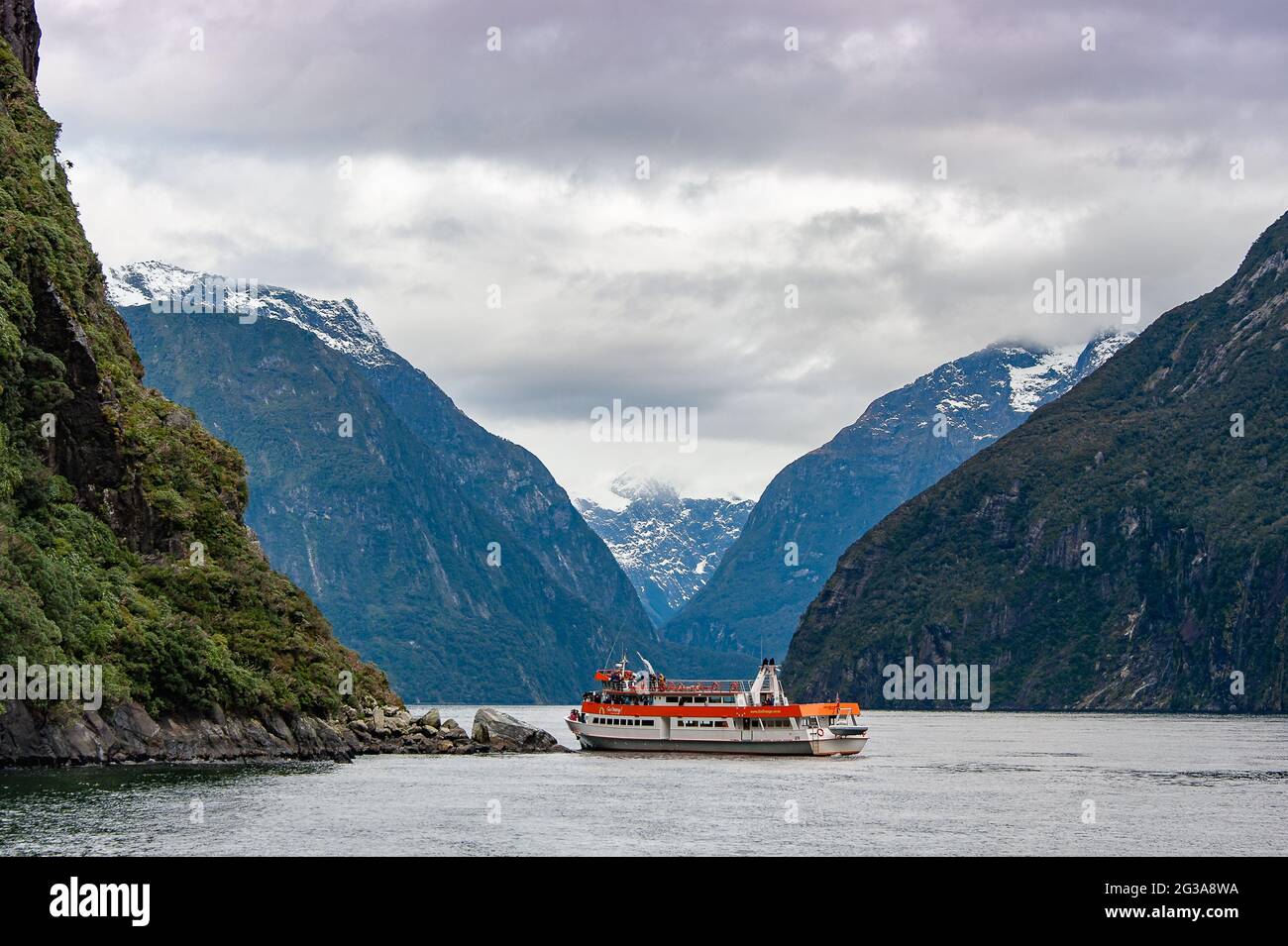 Tourist cruise ship carrying passengers on a scenic cruise through Milford Sound, Fiordland National Park under majestic peaks and a grey, moody sky Stock Photo