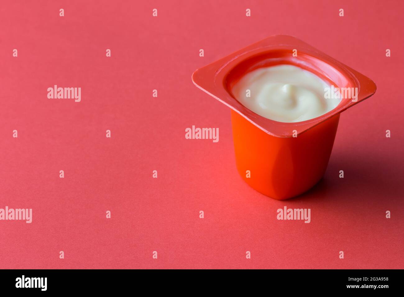 Yogurt cup on red background - delicious fruit yoghurt in red plastic pot with copy space Stock Photo