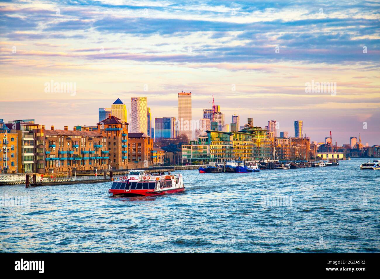 View of East London from Tower Bridge, warehouses of Wapping and Canary Wharf Skyscrapers at sunset, City Cruises tour boat on the Thames river, Londo Stock Photo
