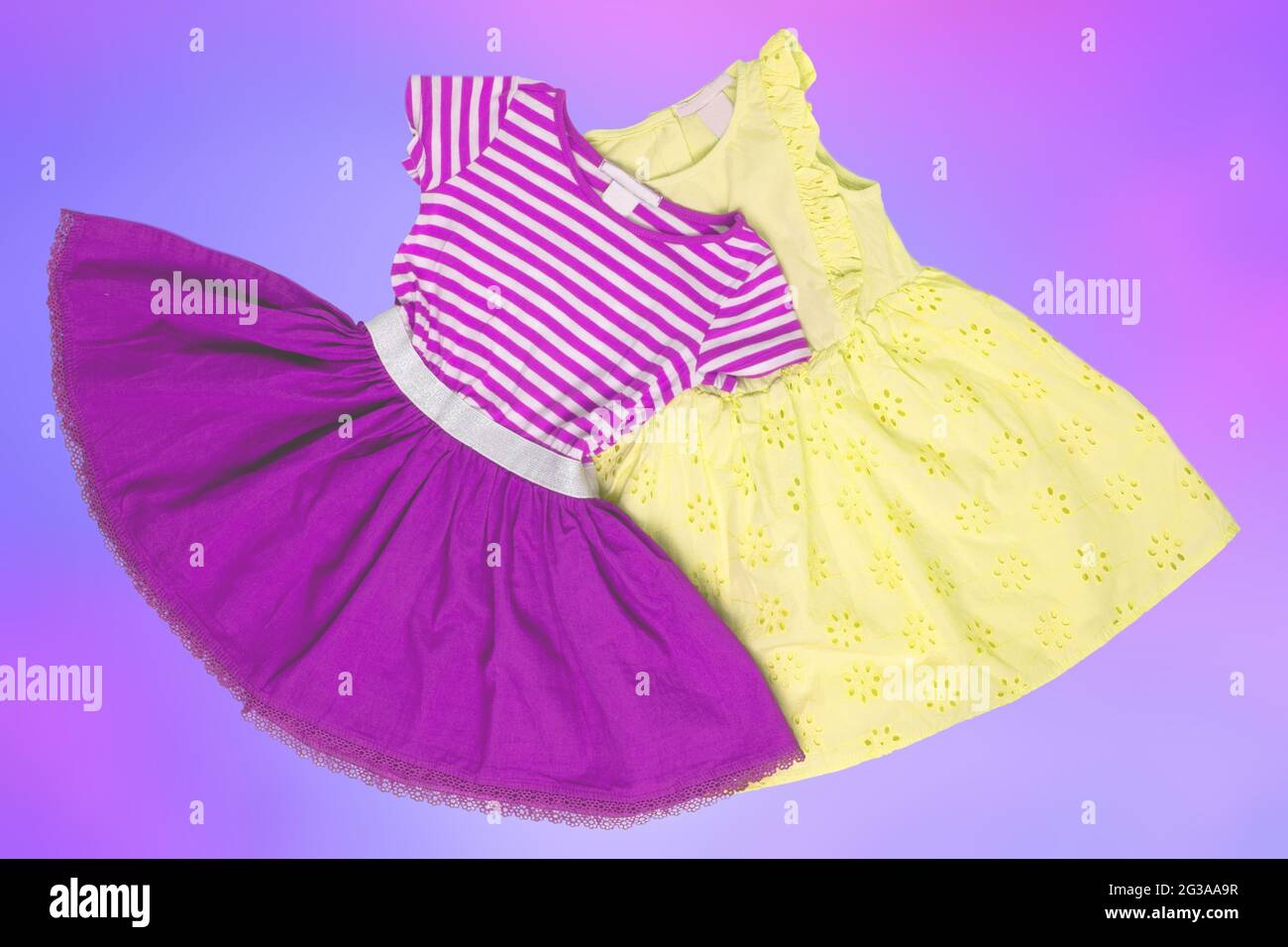 Closeup of a beautiful pink and a yellow sleeveless baby girl dress lying flat from above on an abstract light blue pink background. Space for adverti Stock Photo