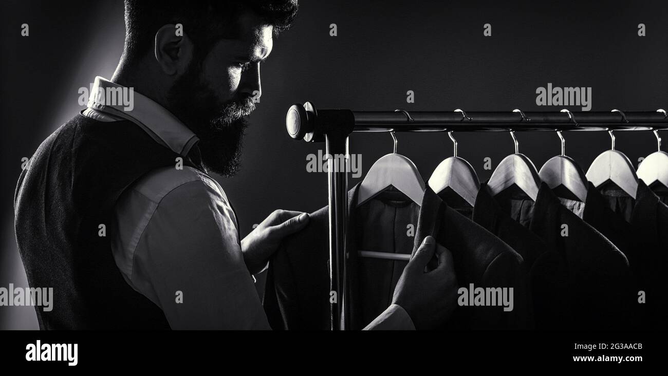 Male suits hanging in a row. Men clothing, boutiques. Tailor, tailoring. Stylish men's suit. Man suit, tailor in his workshop. Handsome bearded Stock Photo