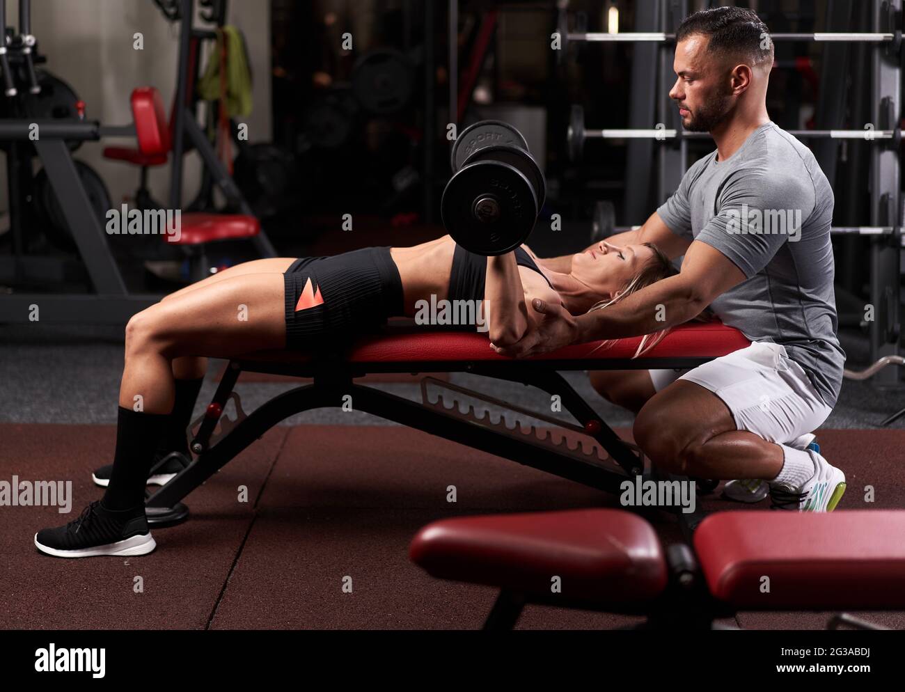 Personal trainer helping a young woman with bench press workout using ...