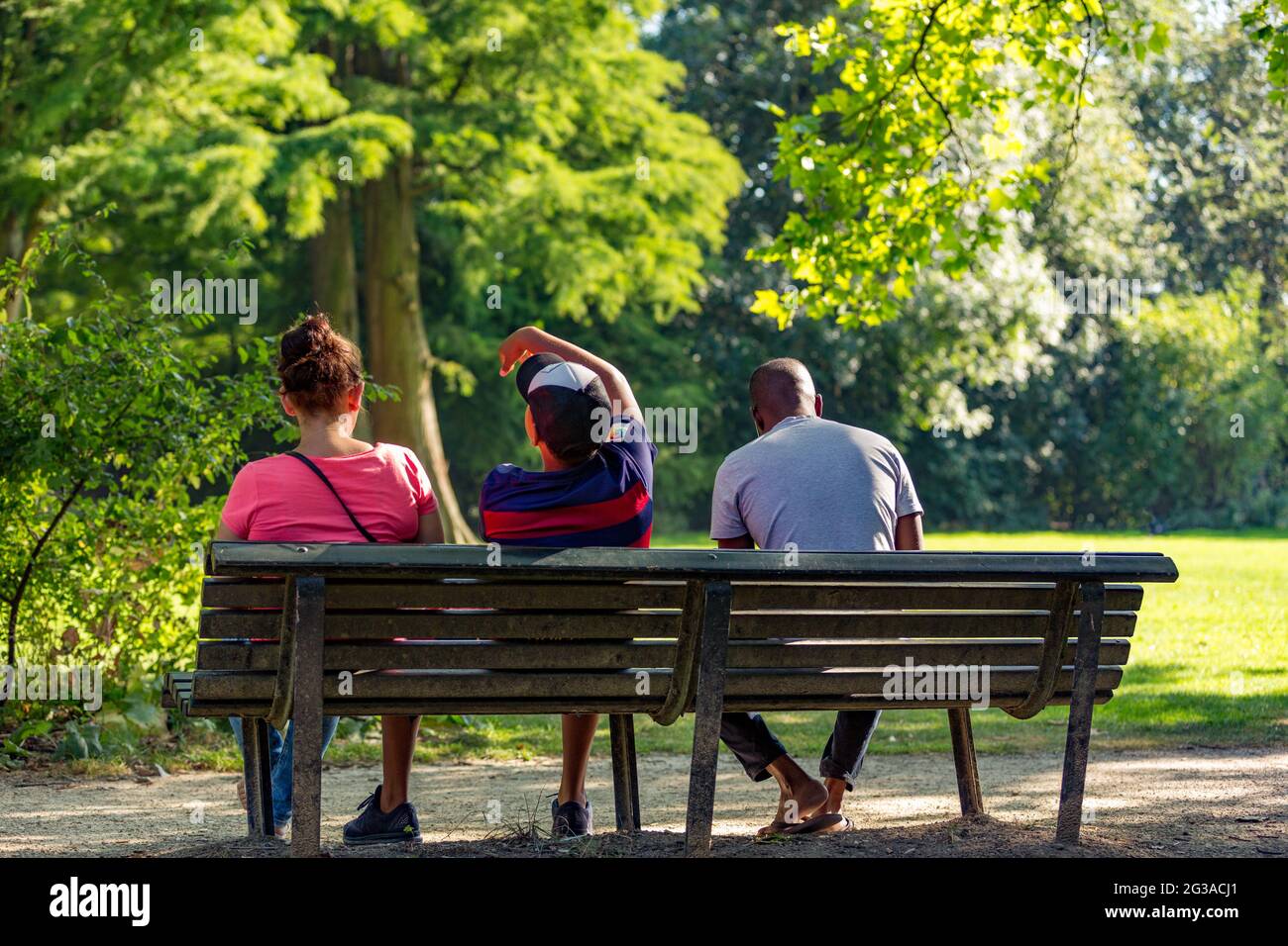 Three people sitting on a bench in a sunny and green Amsterdam Vondelpark in the Netherlands. Stock Photo