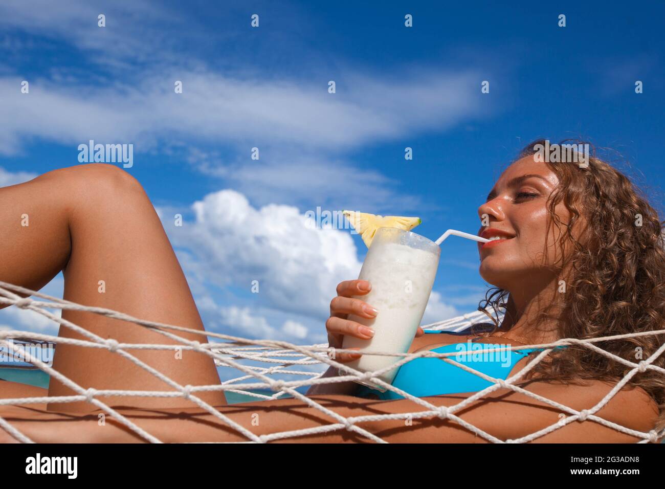 Pretty blonde girl in bikini sitting on hammock with Pina colada cocktail  on the beach Stock Photo - Alamy