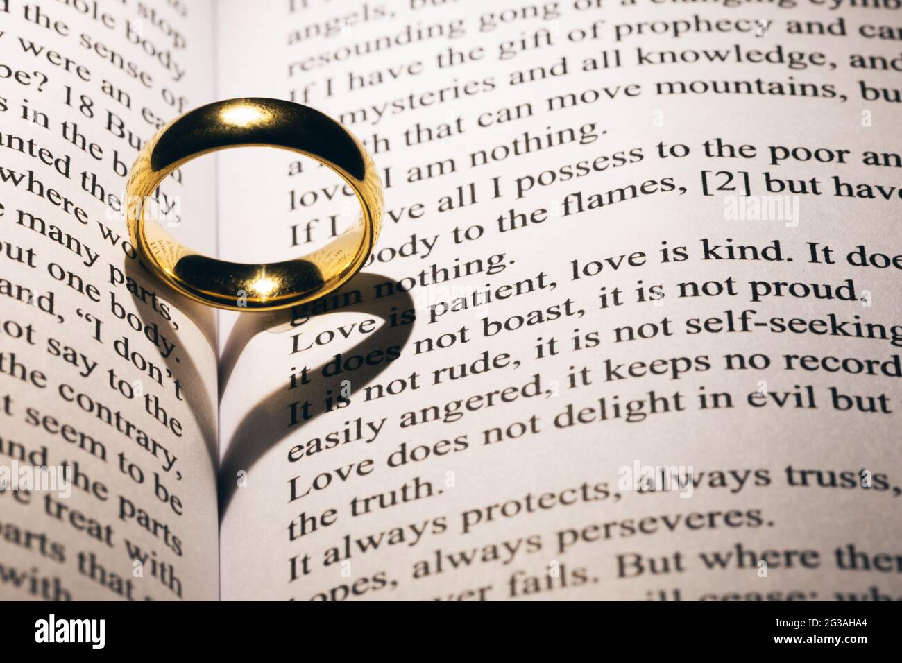 One golden wedding ring on Holy bible book with heart shaped shadow