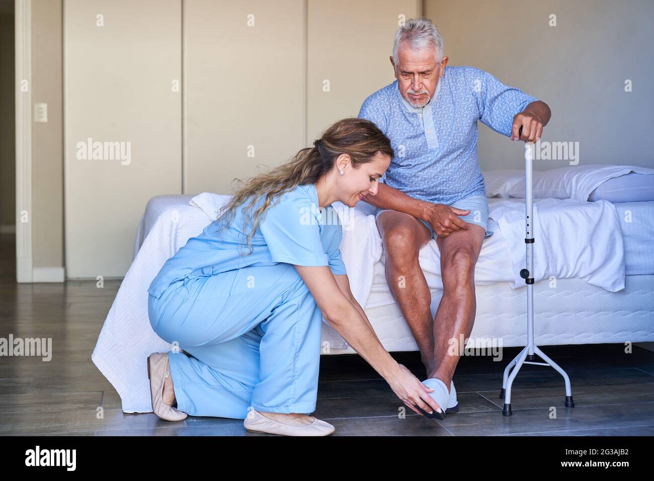 Geriatric nurse helps senior with walking aid to put on shoes in a