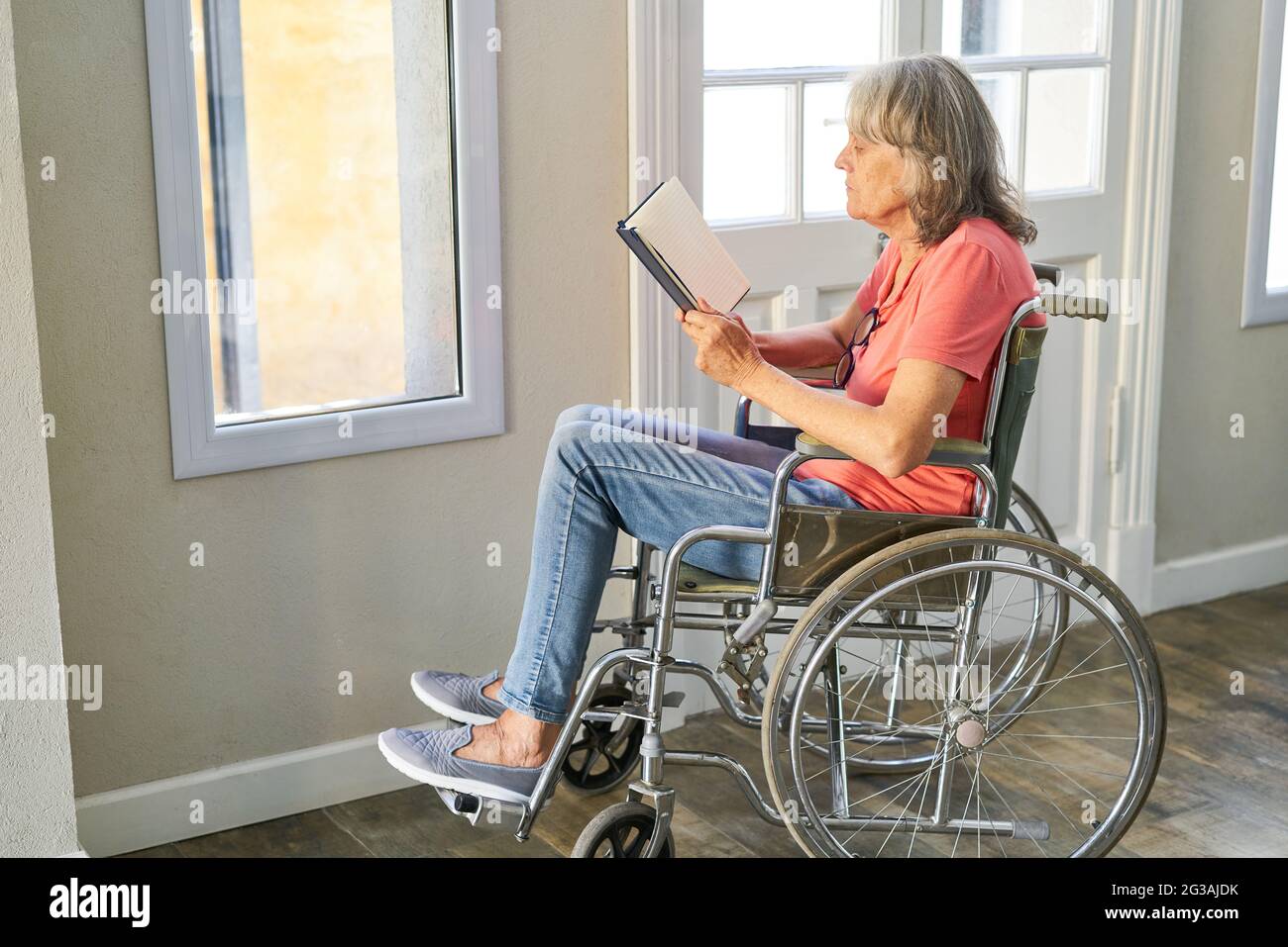Senior woman reading a book in a wheelchair after a stroke at the