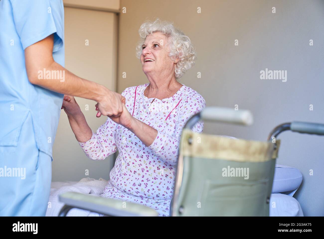 Caregiver helps senior citizens with dementia to get up in the nursing home or retirement home Stock Photo