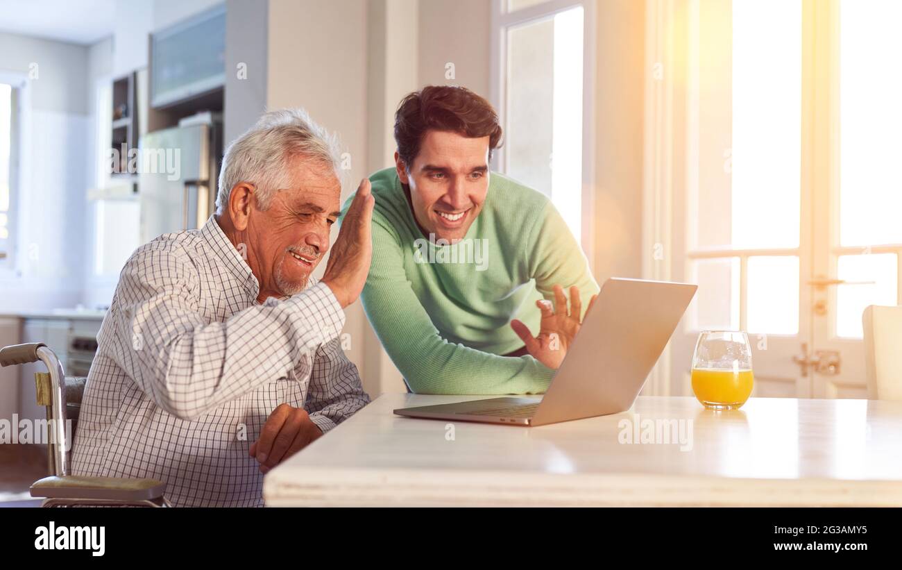 Senior and son waving while video chat on laptop computer with family Stock Photo