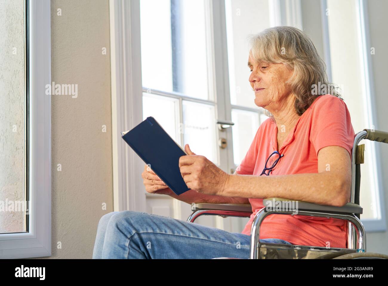 Elderly woman in wheelchair after stroke reading a book in retirement