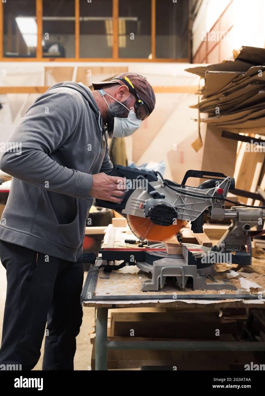 Carpenter with mask and protective glasses cutting a wooden slat with a