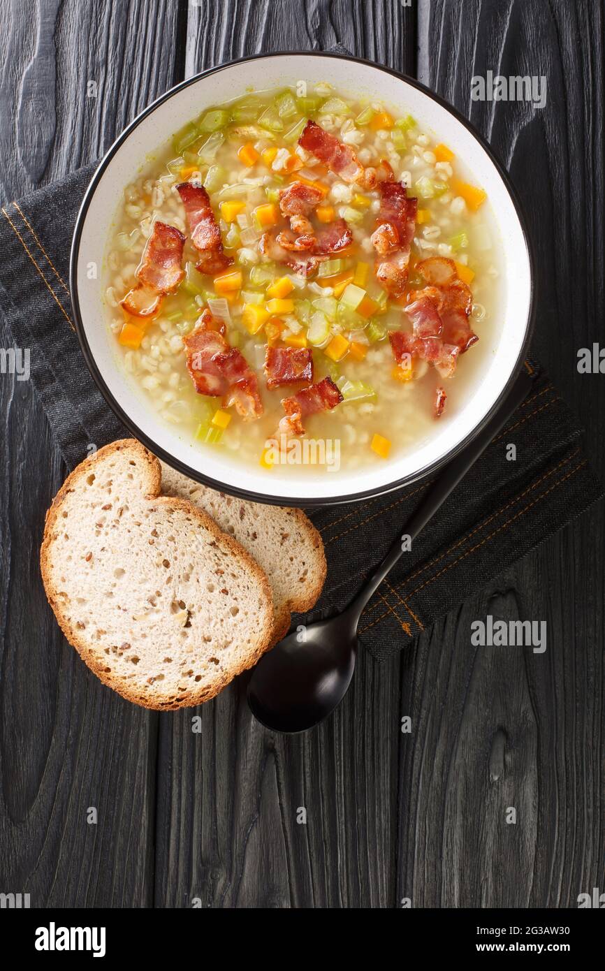Gerstensuppe is a soup made of barley with a few vegetables and a bit of speck close up in the plate on the table. Vertical top view from above Stock Photo