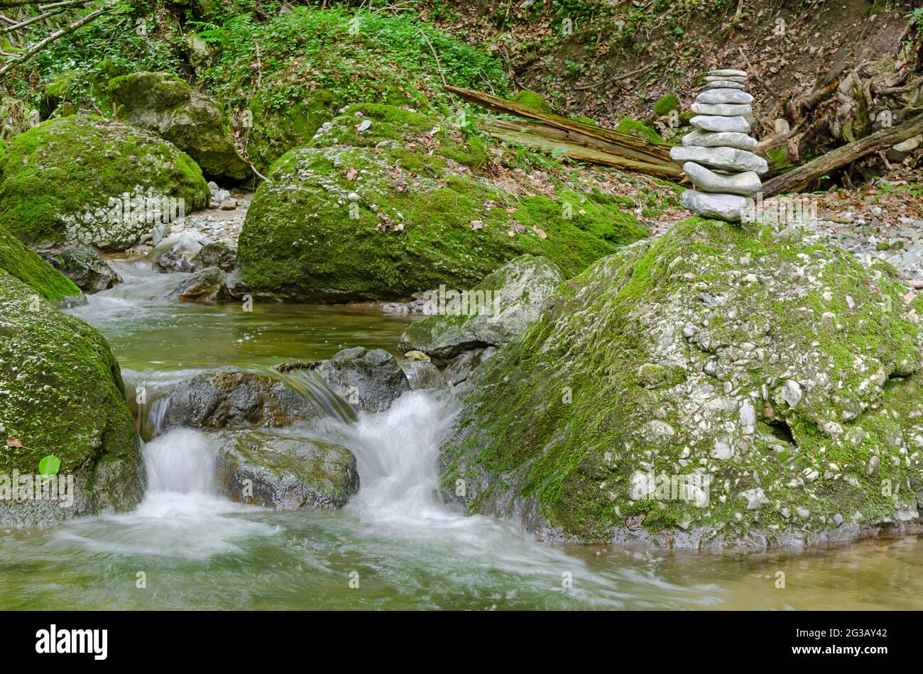 Rock stack, next to a wild stream. Pile of stacked rocks, balancing on a big rock in a streambed. Rocks laid flat upon each other to great height. Stock Photo