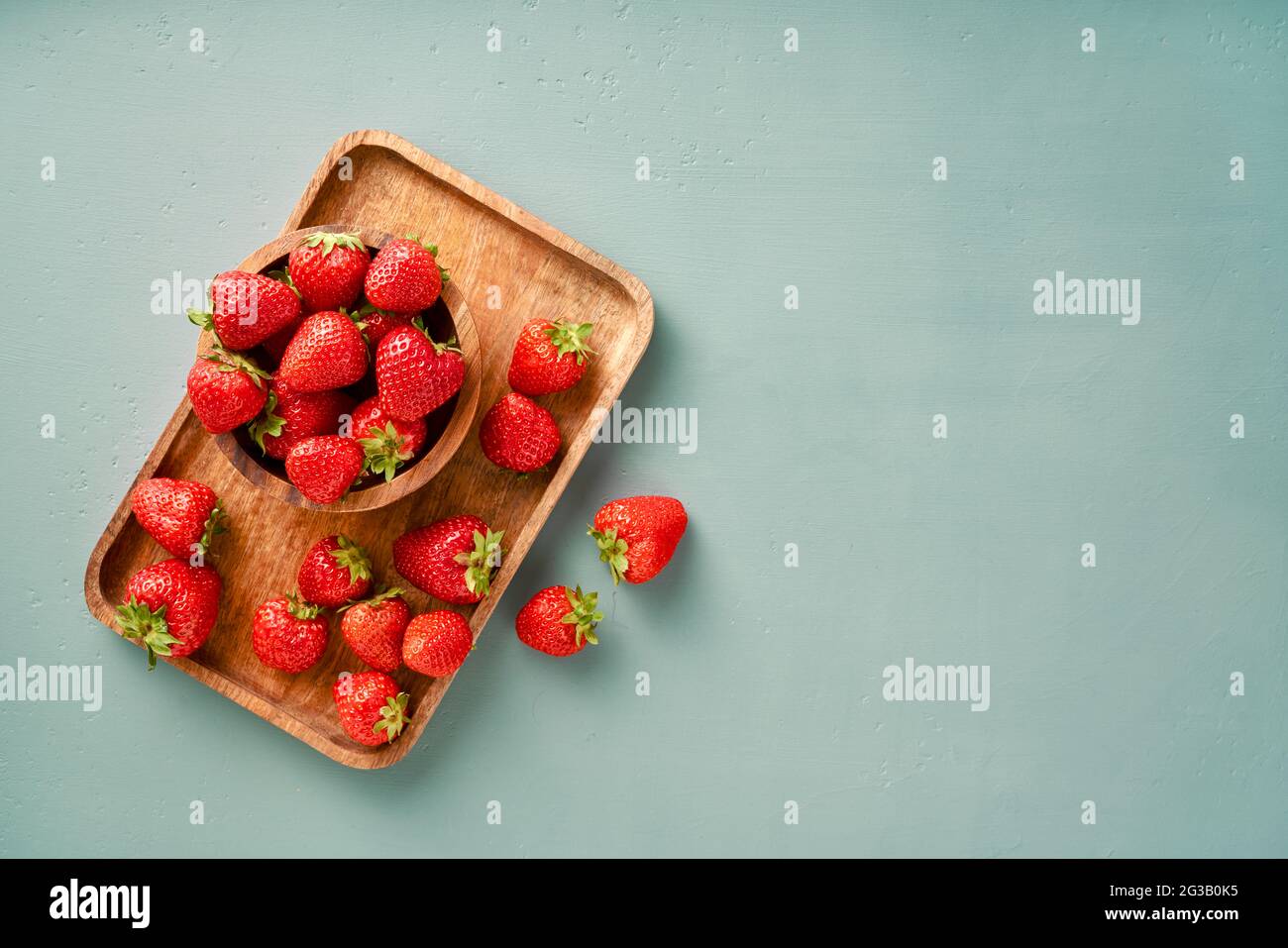 Fresh strawberry on a blue background. Strawberries with leaves on wooden plate. Stock Photo