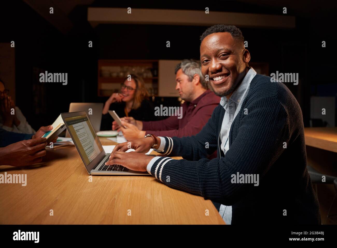 Portrait of smiling young african businessman using his laptop looking at camera while having meeting with his colleague Stock Photo