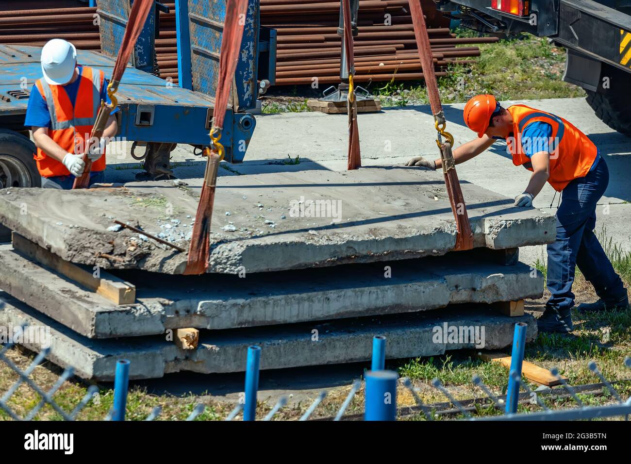 Two slingers unload concrete slabs on the street on a summer day