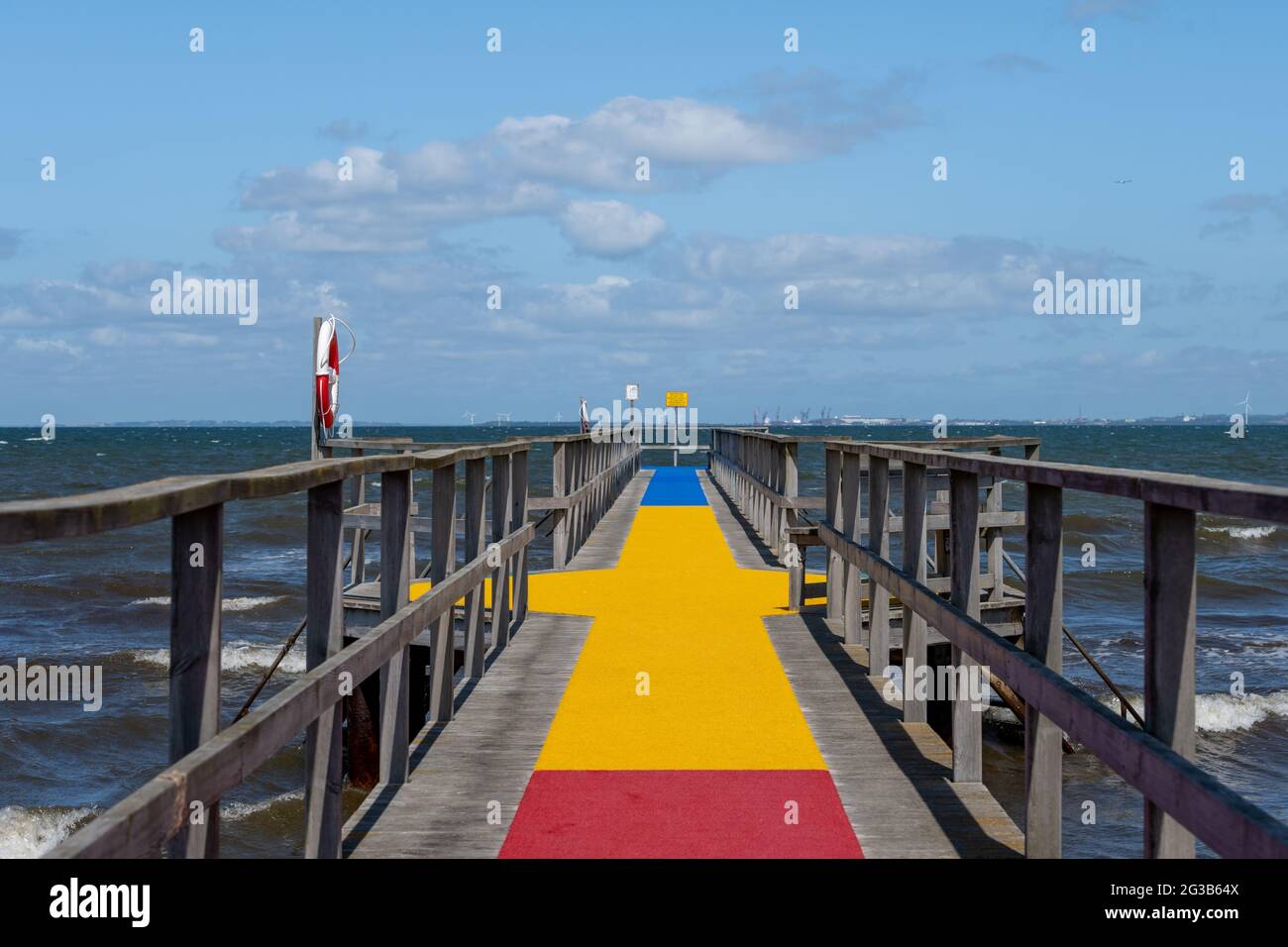 A jetty with a colourful carpet in blue, yellow and red. A blue ocean and sky in the background. Picture from Scania county, Sweden Stock Photo