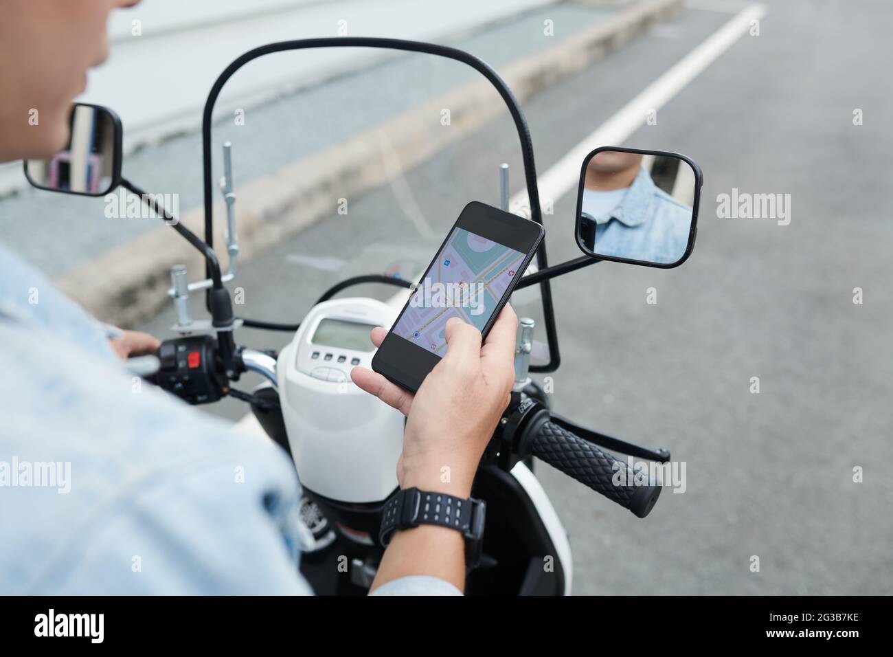 Over shoulder view of man in wristwatch driving moped and using smartphone while navigating with online app Stock Photo
